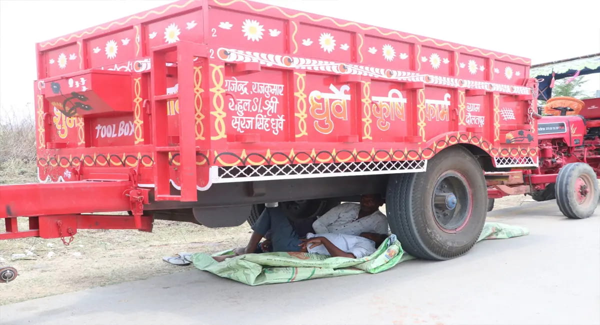 धूप से बचने के लिए ट्रॉलियों के नीचे लेटकर बारी का इंतजार कर रहे किसान